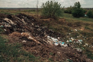 Kırsal kesimde büyük bir çöp yığını. Plastik atıklarla doğanın kirliliği. Çöplerle dolu yeşil arazi. Köydeki pislik yuvası. Etrafa saçılmış çöpler..