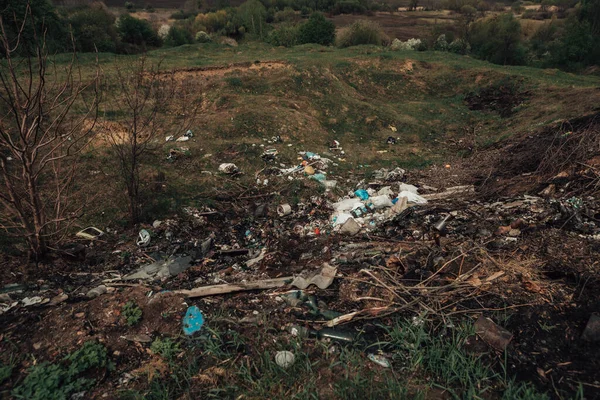Large pile of garbage in the countryside. Pollution of nature with plastic waste. Green land full of rubbish. Dirty trash dump in the village. Scattered litter in the vicinity.
