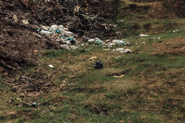 Large pile of garbage in the countryside. Pollution of nature with plastic waste. Green land full of rubbish. Dirty trash dump in the village. Scattered litter in the vicinity.