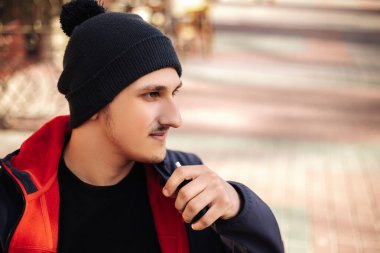 Dışarıda sigara içen genç bir adam var. Elektronik sigara ısıtıcısı. İçinde çubuklar olan duman ve buhar sistemi, fotokopi alanı olan görüntü. Sağlıklı ciğerlere zararlı bir alışkanlık.