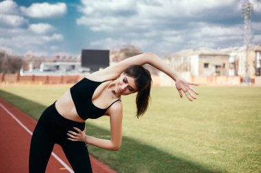 Genç atletik kız esniyor, vücudunu ve kaslarını verimli bir spor koşusu için hazırlıyor. Şehir stadyumunda esnek kadın spor modeli. Kopyalama alanı olan resim.