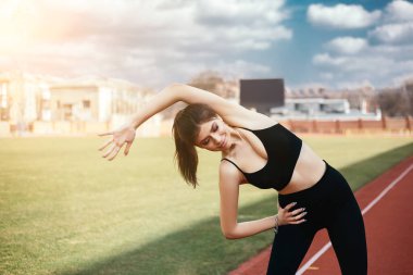 Genç atletik kız esniyor, vücudunu ve kaslarını verimli bir spor koşusu için hazırlıyor. Şehir stadyumunda esnek kadın spor modeli. Kopyalama alanı olan resim.