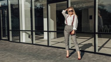 Dışarıda duran ve poz veren genç bir kadın ressamın tam boy portresi. Kendine güvenen pantolon askısı olan lüks takım elbiseli güzel bir kadın. Küçük işletme sahibi, girişimci, avukat. Boşluğu kopyala.
