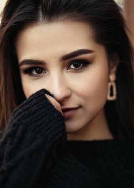 Genç Hintli kadının dikey portresi soğuktur. Hava bulutlu, siyah kazak giymiş ve kameraya bakıyor.. 