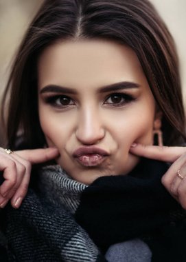 Genç Hintli bir kadının dikey portresi. Sokakta durmuş, komik suratlar yapıyor, yüzünü buruşturuyor, kameraya bakıyor..