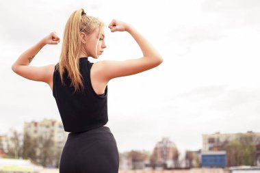 Kaslarını gösteren genç bir kadının yan görünüşü mükemmel formda güçlü, entrikacı bir kadın kameraya bakıyor. Çekici spor aktiviteleri sağlık hizmetleri konsepti.