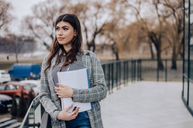 Küçük işletme sahibi ofis çalışanı kadın elinde belgelerle binanın dışında duruyor, gülümsüyor. Meksikalı kadın, Latin Amerikalı başarılı yönetici kız, iş arkadaşıyla buluşuyor. Boşluğu kopyala.
