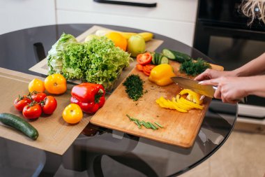 Yakından çekilen kadın mutfakta el ele tutuşuyor. Sarı biber ürünleri sebze, ahşap kesme tahtası. Eğitimden sonra kahvaltı hazırlayan bir kadın, sağlıklı yemek ve mekan istiyor..