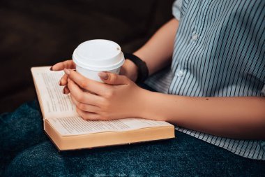 Kafe 'de oturan beyaz kadın, plastik bardak sıcak içecek içer, kahve molası verir, kucak üzerinde el kitabı tutar, rahatça kitap okur, rahatça bilgi kurgusu kurgular. Çizgili tişörtlü bayan. Taklit alan.