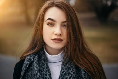 Kameraya bakan kızıl kadının yatay yakın plan portresi. Çekici, güzel gözleri olan, soğuk sonbahar doğası bulanık bokeh arka planı olan genç bir bayan. Koyu renk ceket giyen kız.