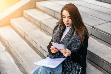Beton merdivenlerde oturan bir kadın, okuyun tablet bilgisayar belgelerini kullanın iş sözleşmesi için devam edin. İş arayan bir kadın. Küçük bir işletme sahibi, ortak alan. Serbest Çalışan çevrimiçi ders notları alıyor