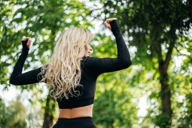 Arkadan bakan kadın Green Park 'ın dışında kaslarını gösteren pozlar veriyor. Spor kıyafetleri giymiş atletik bir bayan. Sağlıklı yaşam tarzı, spor eğlencesi. Boşluğu kopyala