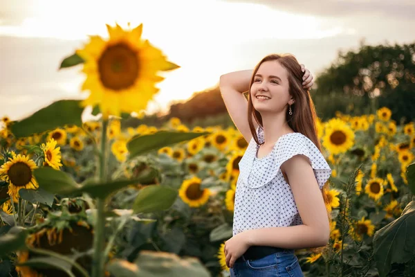 Sevimli, çekici bir genç kız sarı buket çiçeklerin açtığı açık hava günbatımı, sıcak doğa arka planında yürüyor. Kadın hafta sonu seyahat ederken durdu. Yaz tatili