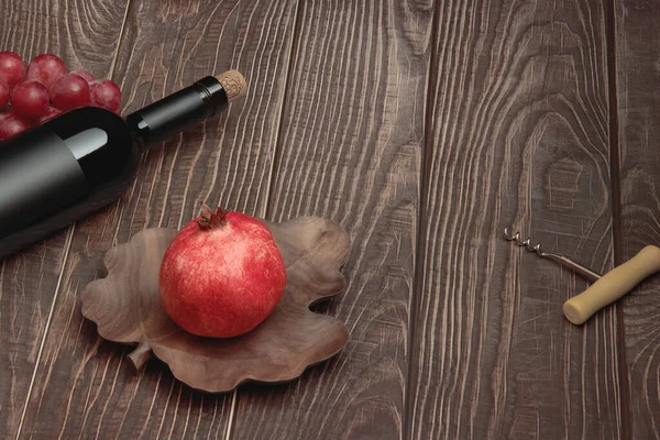 Expensive wine bottle with corkscrew, pomegranate and grapes on textured wooden table background