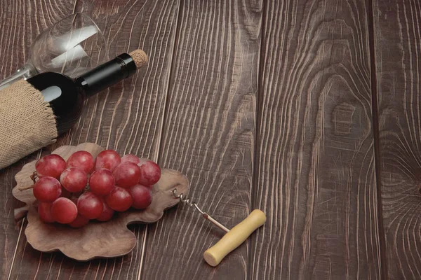 Expensive wine bottle with corkscrew and grapes on conceptual wooden boards background