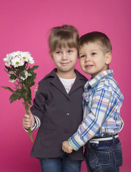 Kleines Mädchen umarmt einen Jungen mit Blumen — Stockfoto