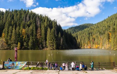 Lakul Rosu, Romanya 'nın Doğu Karpatya Dağları' ndaki çarpıcı bir baraj gölü. Bereketli ormanlar, sonbahar renkleri ve bulutlu mavi gökyüzü.