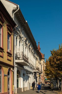 Targu Mures, Romanya - Ekim 17.2025. Romanya 'nın Targu Mures kentinin tarihi merkezinde, parlak mavi gökyüzü altında süslü binalar, sokak parkı, trafik ve sonbahar ağaçlarının yer aldığı bir sokak manzarası