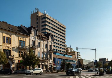 Targu Mures, Romanya - Ekim 17.2025. Romanya 'nın Targu Mures kentinin tarihi merkezinde, parlak mavi gökyüzü altında süslü binalar, sokak parkı, trafik ve sonbahar ağaçlarının yer aldığı bir sokak manzarası