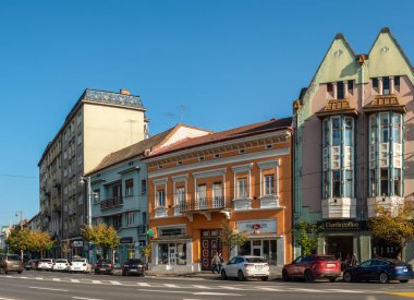 Targu Mures, Romanya - Ekim 17.2025. Romanya 'nın Targu Mures kentinin tarihi merkezinde, parlak mavi gökyüzü altında süslü binalar, sokak parkı, trafik ve sonbahar ağaçlarının yer aldığı bir sokak manzarası