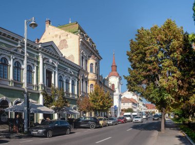 Targu Mures, Romanya - Ekim 17.2025. Romanya 'nın Targu Mures kentinin tarihi merkezinde, parlak mavi gökyüzü altında süslü binalar, sokak parkı, trafik ve sonbahar ağaçlarının yer aldığı bir sokak manzarası
