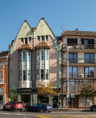 Targu Mures, Romanya - Ekim 17.2025. Romanya 'nın Targu Mures kentinin tarihi merkezinde, parlak mavi gökyüzü altında süslü binalar, sokak parkı, trafik ve sonbahar ağaçlarının yer aldığı bir sokak manzarası