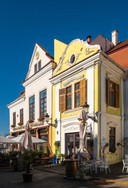 Medya, Romanya - Ekim 20.2025. Romanya 'nın Medias kentinde klasik Sakson mimarisi, kırmızı kiremitli çatılar ve park halindeki arabalarla renkli tarihi cephelerin yer aldığı bir caddenin güneşli perspektifi