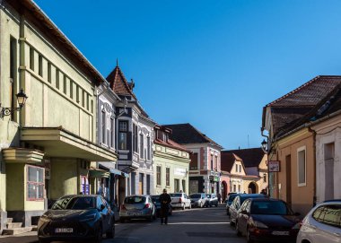 Medya, Romanya - Ekim 20.2025. Romanya 'nın Medias kentinde klasik Sakson mimarisi, kırmızı kiremitli çatılar ve park halindeki arabalarla renkli tarihi cephelerin yer aldığı bir caddenin güneşli perspektifi