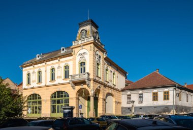 Medya, Romanya - Ekim 20.2025. Romanya 'nın Medias kentinde klasik Sakson mimarisi, kırmızı kiremitli çatılar ve park halindeki arabalarla renkli tarihi cephelerin yer aldığı bir caddenin güneşli perspektifi