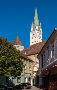 Medya, Romanya - 20.2025. Sembolik St. Margaret Kilisesi saat kulesi ve renkli kulesi, Medias 'taki huzurlu bir park ve kasaba meydanına bakıyor.