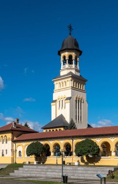 Alba Iulia, Romanya - Ekim 19.2025. Alba Iulia Romanya 'daki açık mavi gökyüzünün altında, kemerli sarı bir portonun arkasındaki taç giyme töreninin kuleleri yükseliyor.