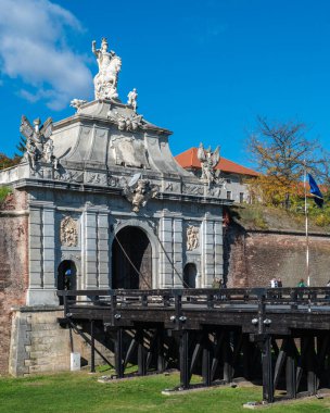 Alba Iulia, Romanya - Ekim 19.2025. Romanya 'daki Alba Carolina Kalesi' ndeki tarihi ahşap köprünün sonunda heykeli olan süslü bir barok taş kapı duruyor.