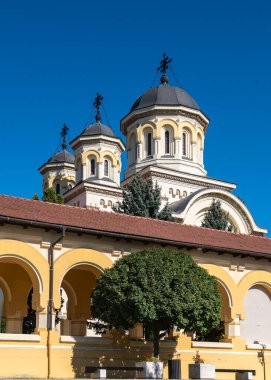 Alba Iulia, Romanya - Ekim 19.2025. Alba Iulia Romanya 'daki açık mavi gökyüzünün altında, kemerli sarı bir portonun arkasındaki taç giyme töreninin kuleleri yükseliyor.