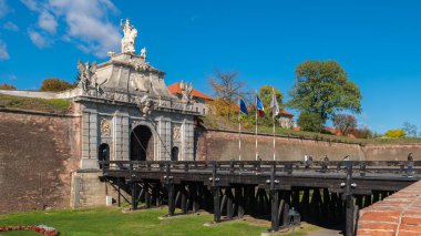 Alba Iulia, Romanya - Ekim 19.2025. Romanya 'daki Alba Carolina Kalesi' ndeki tarihi ahşap köprünün sonunda heykeli olan süslü bir barok taş kapı duruyor.