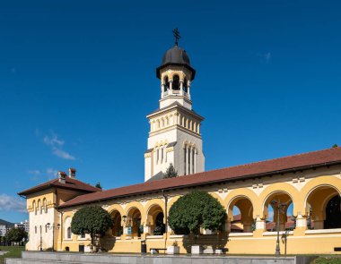 Alba Iulia, Romanya - Ekim 19.2025. Alba Iulia Romanya 'daki açık mavi gökyüzünün altında, kemerli sarı bir portonun arkasındaki taç giyme töreninin kuleleri yükseliyor.