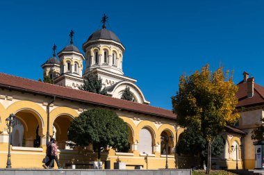 Alba Iulia, Romanya - Ekim 19.2025. Alba Iulia Romanya 'daki açık mavi gökyüzünün altında, kemerli sarı bir portonun arkasındaki taç giyme töreninin kuleleri yükseliyor.