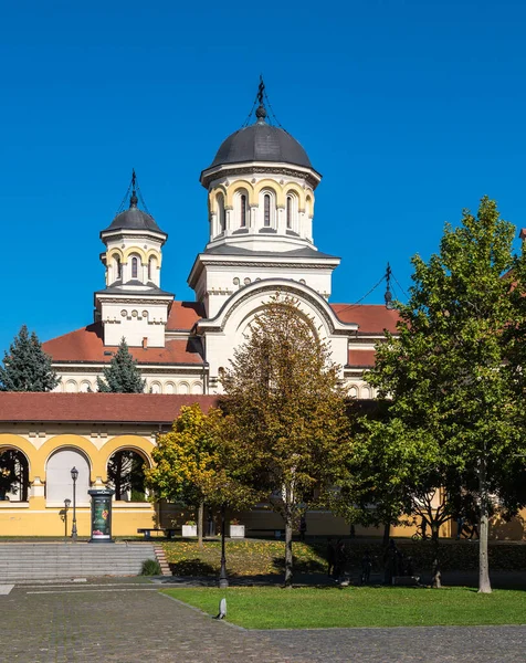 Alba Iulia, Romanya - Ekim 19.2025. Alba Iulia Romanya 'daki açık mavi gökyüzünün altında, kemerli sarı bir portonun arkasındaki taç giyme töreninin kuleleri yükseliyor.