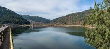 Romanya 'nın Neamt bölgesinde güneşli bir sonbahar gününde İzvorul Muntelui Gölü' nün sakin manzarası, çamlarla kaplı Karpat Dağları 'nı yansıtıyor