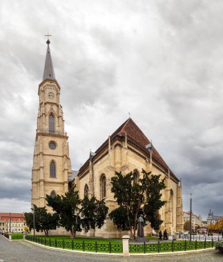 Cluj-Napoca, Romanya - Ekim 18.2025. Gotik St. Michael Kilisesi ve merkez Union Square of Cluj-Napoca 'daki Matthias Corvinus Heykel Grubu' nun gri gökyüzü altında geniş bir manzarası vardır.