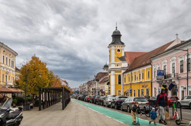 Cluj-Napoca, Romanya - Ekim 18.2025. Romanya 'nın Cluj-Napoca kentindeki Eroilor Bulvarı' nda tarihi binalar, yeşil boyalı bisiklet şeridi ve dramatik bulutlu gökyüzü altında elektrikli scooterlar bulunuyor.