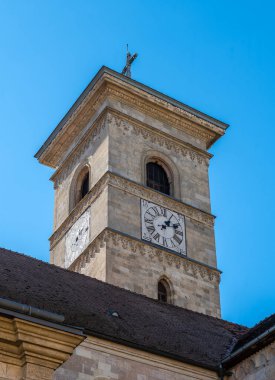 Alba Iulia, Romanya - Ekim 19.2025. St. Michaels Katedrali 'nin tarihi taş saat kulesinin yakın plan bir resmi. Açık mavi gökyüzüne karşı ortaçağ oymaları ve beyaz bir saat yüzü sergileniyor.
