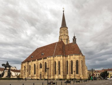 Cluj-Napoca, Romanya - Ekim 18.2025 Gotik St. Michael Kilisesi ve merkezdeki Cluj-Napoca Union Meydanı 'ndaki Matthias Corvinus Heykel Grubu gri bir gökyüzü altında