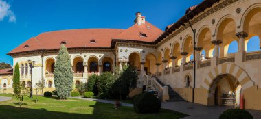 Alba Iulia, Romanya - Ekim 19.2025. İç avlunun sakin manzarası kemerli galeriler, manikürlü yeşillik ve taç giyme törenindeki geleneksel mimari.