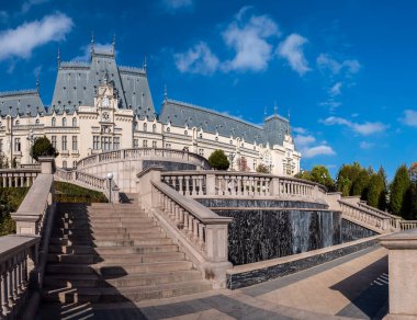 Iasi, Romanya - 23 Ekim 2025. Iasi Romanya 'daki Neo-Gotik Kültür Sarayı' nın geniş panoramik manzarasında, parlak mavi gökyüzü altında fıskiyeler ve sonbahar ağaçları bulunan bereketli Palas Halk Bahçesi yer alıyor.