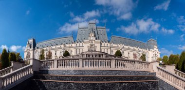 Iasi, Romanya - 23 Ekim 2025. Iasi Romanya 'daki Neo-Gotik Kültür Sarayı' nın geniş panoramik manzarasında, parlak mavi gökyüzü altında fıskiyeler ve sonbahar ağaçları bulunan bereketli Palas Halk Bahçesi yer alıyor.