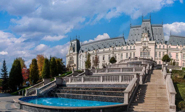 Iasi, Romanya - 23 Ekim 2025. Iasi Romanya 'daki Neo-Gotik Kültür Sarayı' nın geniş panoramik manzarasında, parlak mavi gökyüzü altında fıskiyeler ve sonbahar ağaçları bulunan bereketli Palas Halk Bahçesi yer alıyor.