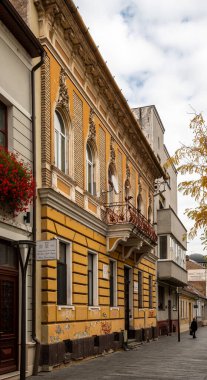 Cluj-Napoca, Romanya - Ekim 18.2025. Cluj-Napoca 'daki zarif sarı tarihi bina cephesinde kemerli pencereler, dekoratif süsler ve işlenmiş demir bir balkon yer alıyor.