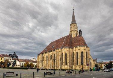 Cluj-Napoca, Romanya - Ekim 18.2025 Gotik St. Michael Kilisesi ve merkezdeki Cluj-Napoca Union Meydanı 'ndaki Matthias Corvinus Heykel Grubu gri bir gökyüzü altında