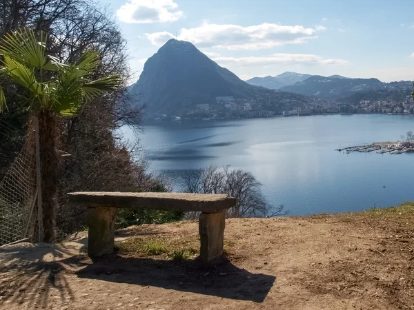ม้านั่งหินอ่อนที่มองเห็นอ่าว Lugano และภูเขา San Salvat — ภาพถ่ายสต็อก