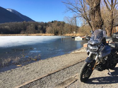 Carlazzo, İtalya 7 Temmuz 2019: Park etmiş bir motosikletle yarı donmuş Piyano Gölü.